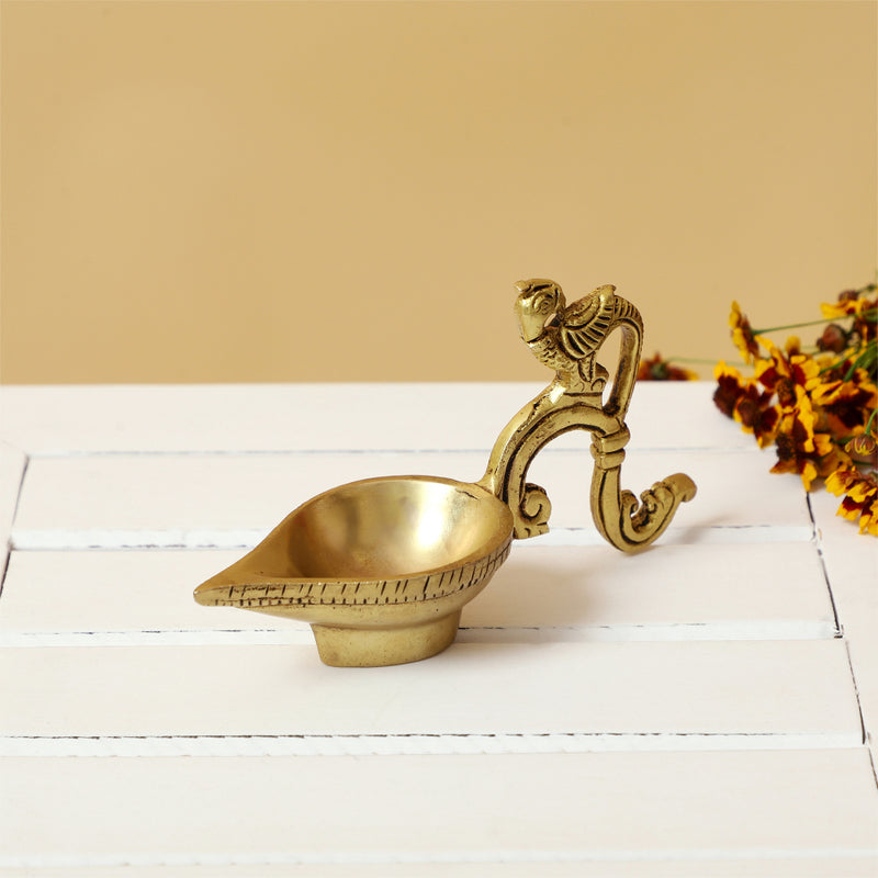 Brass peacock parrot Diya - exquisitely crafted brass oil lamp in the shape of a peacock with parrot motifs, golden finish, decorative home accent, fusion of elegance and vibrancy, traditional Indian Diya, emits a captivating and auspicious glow, perfect for festive occasions and religious ceremonies, enhances spiritual ambiance and decor with a touch of artistic brilliance.